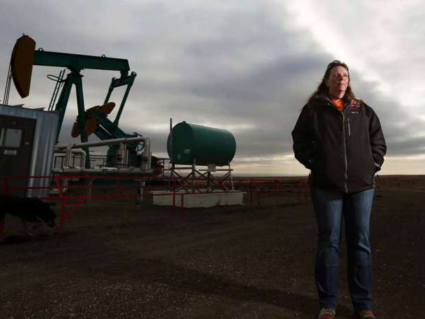 Kelly Nelson stands near an oil pump jack on the farm she owns with her husband, Gord, east of Arrowwood, Alberta.